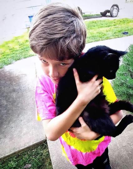 Beautiful Mewpers the black cat is held by my son Lennon in a bright tie-dye shirt in 2018. R.I.P. Mewpers, who left the Earth this evening.